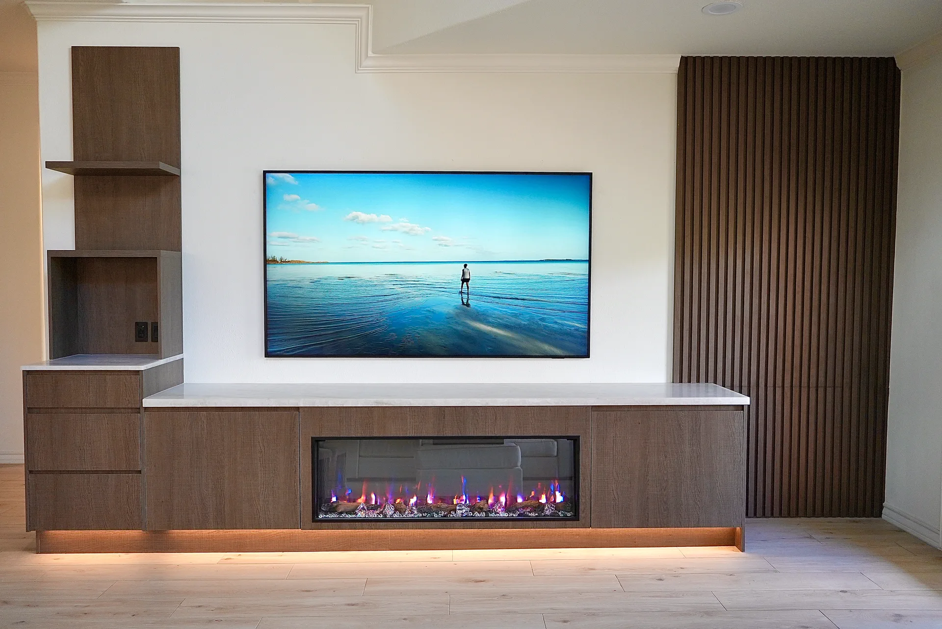 Custom-home media wall with built-in storage, fireplace, floating shelves, and fluted wood panels